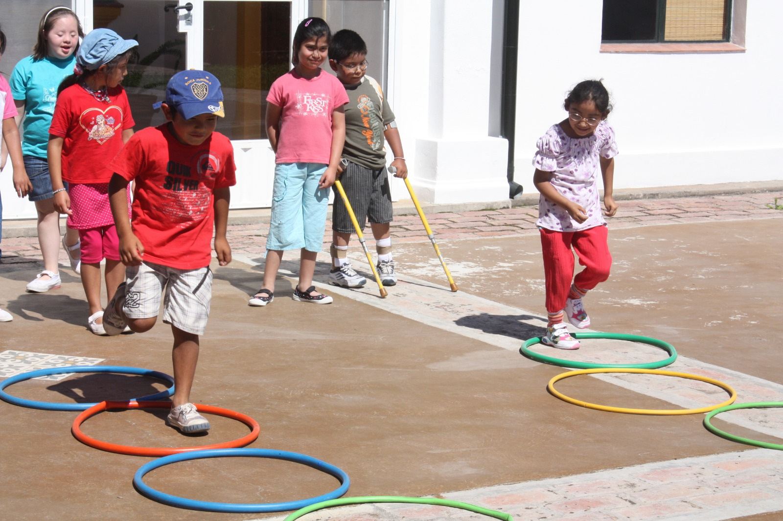 Un chico salta entre aros de colores en el patio mientras sus compañeros miran.